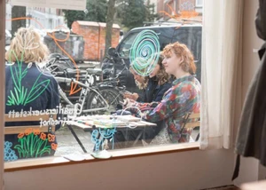 Menschen vor dem Fenster der Quartierswerkstatt, die an einem Tisch sitzen