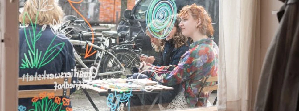 Menschen vor dem Fenster der Quartierswerkstatt, die an einem Tisch sitzen