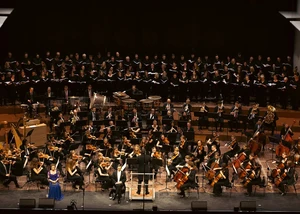 Ein Orchester mit einem Chor auf einer großen Bühne, die gerade einen Auftritt haben