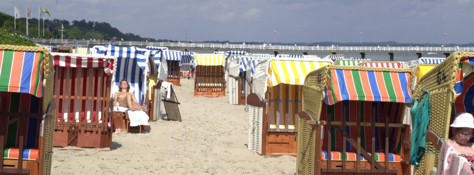 Strandkörbe und Seebrücke am Ostseestrand. Reihen von bunten Strandkörben am Sandstrand mit Blick auf die Ostsee und eine lange Seebrücke.