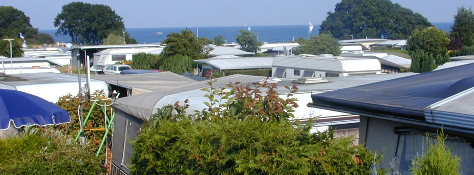 Campingplatz an der Ostsee mit Wohnwagen, Meerblick und grünen Hecken bei Sommerwetter.