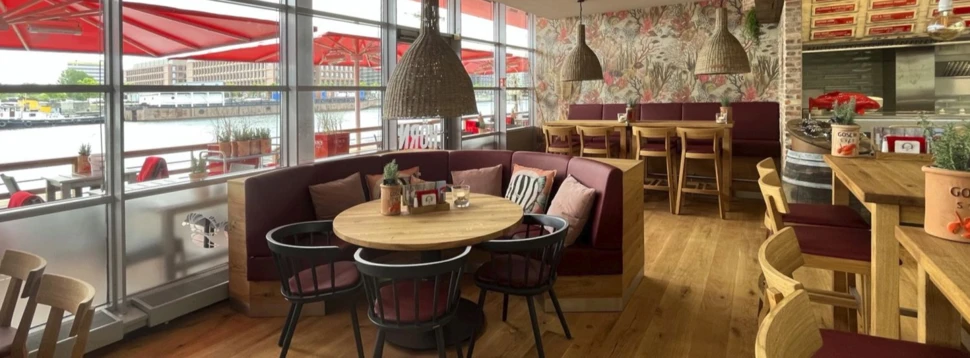 Innenraum eines Fischrestaurants mit roten Polstern, Holzmöbeln, maritimer Dekoration und großen Panoramafenstern zum Hafen.