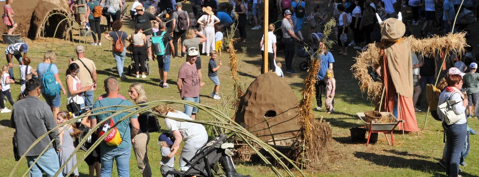 Menschen auf einem Outdoor Festival mit Strohfiguren und Mitmachaktionen auf einer Wiese