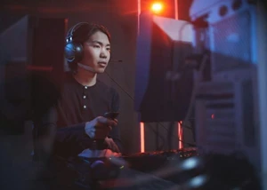 Mann sitzt in einem dunklem Raum vor einem PC und hält ein Kontroller in der Hand