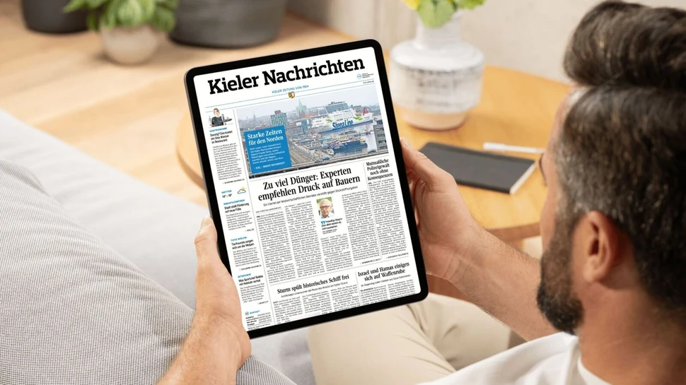 ein Mann sitzt auf einem Sofa und liest das E-Paper der Kieler Nachrichten