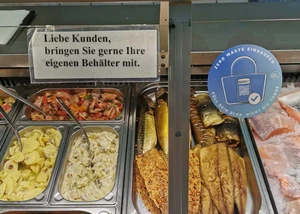 Ein blauer Aufkleber eines Kieler Vereins, der an der Scheibe eines Fischhändlers angebracht ist und auf eine Kampagne zur Müllvermeidung hinweist