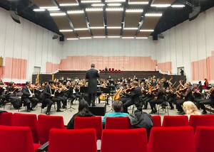Mehrere Menschen in einem großen Raum mit roten Sitzen und Instrumenten in der Hand