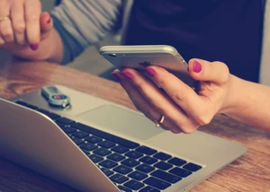 Frau mit rosa Nagellack hält Smartphone über Laptop-Tastatur