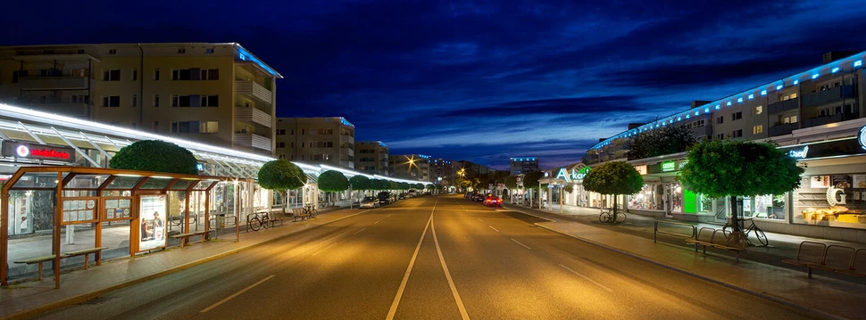 Leere Holtenauer Straße bei Nacht mit beleuchteten Geschäften, Wohnblocks und dramatischem blauen Himmel