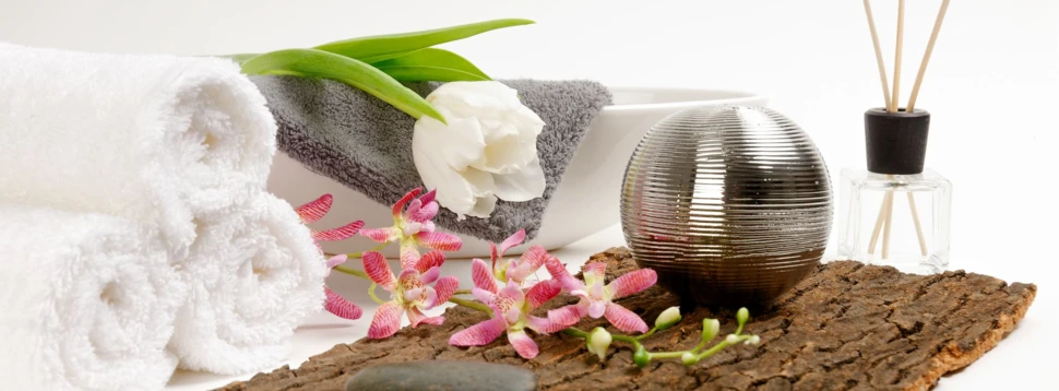 Handtücher, Blumen, Holz und Duftstäbchen vor einer weißen Wand