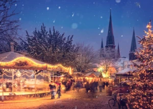 Weihnachtsmarkt Ein Weihnachtsmarkt in einer verschneiten Stadt mit Lichterketten an den einzelnen Buden und Kirchtürmen im Hintergrund