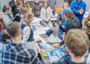 Viele Jugendliche stehen um einen langen Tisch auf dem zahlreiche künstlerische Arbeiten liegen