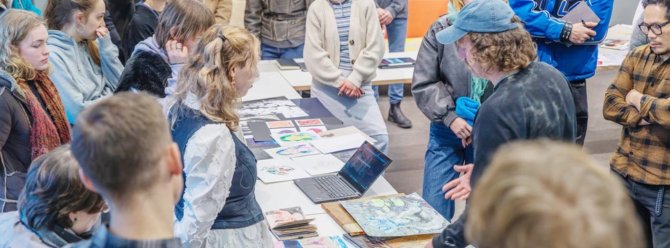 Viele Jugendliche stehen um einen langen Tisch auf dem zahlreiche künstlerische Arbeiten liegen
