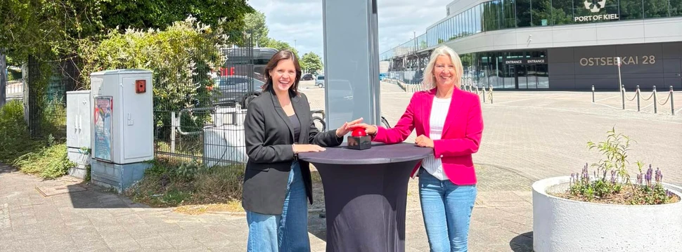 Zwei Frauen vor einem mit schwarzer Decke, auf dem ein roter Buzzer steht, mit dem ein neues kostenloses Kulturangebot hingewiesen wird