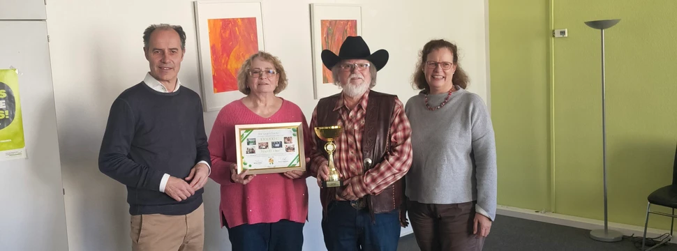 Vier Menschen vor einer weißen Wand, die gerade eine Urkunde und einen Pokal übergeben bzw. erhalten haben