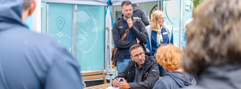 OB Yilmaz beim Austausch mit Menschen vor Ort während seiner Tour mit dem Tiny-Rathaus im Hintergrund