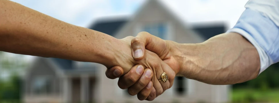 Handschlag von zwei Händen, im Hintergrund ein Haus
