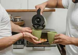 Zwei grüne Becher Kaffee, in die aus einer Kaffeekanne Kaffee gefüllt wird