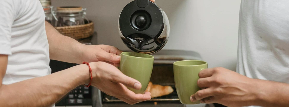 Zwei grüne Becher Kaffee, in die aus einer Kaffeekanne Kaffee gefüllt wird