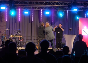 Drei Menschen auf einer Bühne vor Publikum, die gerade ein Foto machen