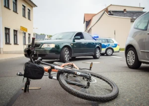 Umgestürztes Fahrrad auf Straße nach Verkehrsunfall mit Polizeiauto im Hintergrund.