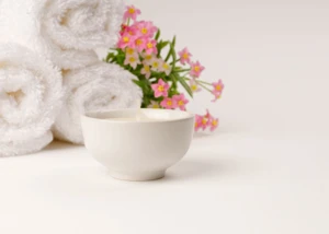 Ruhe und Entspannung mit Duftkerze und Blüten im Spa-Stil. Duftkerze mit weißen Handtüchern und pinken Blumen in ruhiger Spa-Atmosphäre.