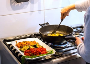 Zubereitung von mediterranem Gemüse in einer modernen Küche. Eine Person brät Zucchini in einer Pfanne, während eine Gemüseplatte mit gegrilltem Gemüse bereitsteht.