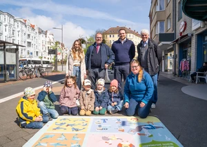 Vier Erwachsene und sechs Kinder posieren auf der Straße, auf dem Boden ein Spielepunkt