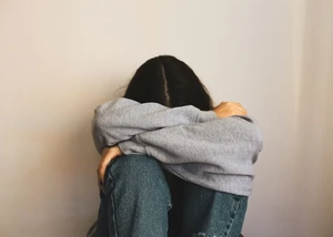 Mädchen sitzt an einer Wand. Hände sind um ihren Körper. Ihr Kopf liegt in ihren Armen.