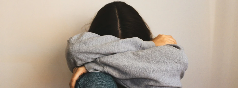 Mädchen sitzt an einer Wand. Hände sind um ihren Körper. Ihr Kopf liegt in ihren Armen.