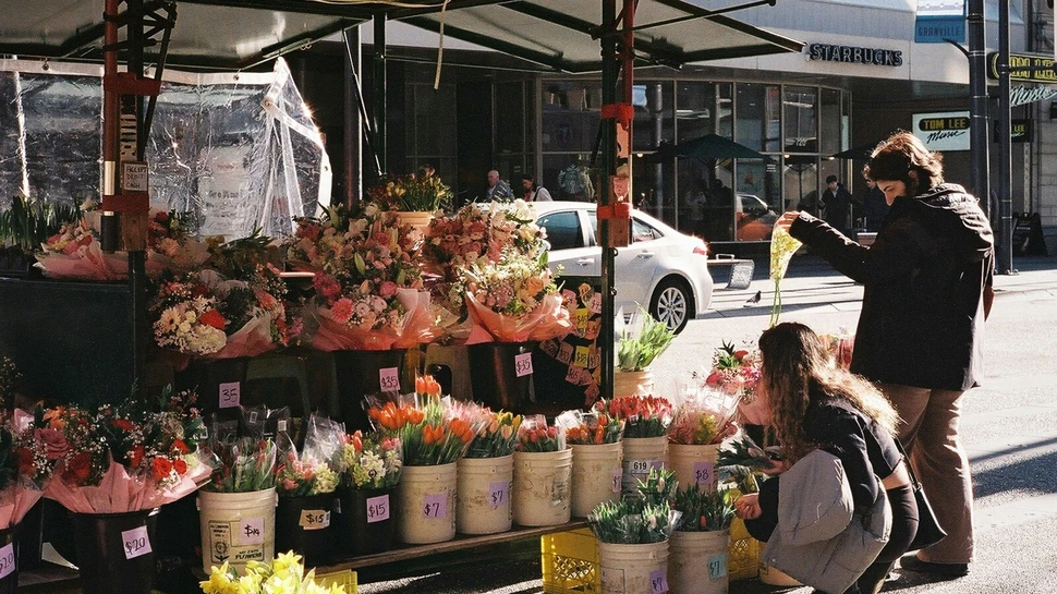 Blumenstand auf der Straße. Zwei Kunden schauen sich die Blumensträuße an.