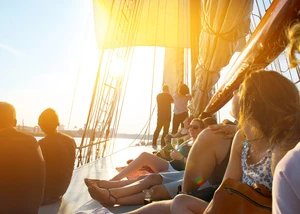 auf dem Deck eines Segelschiffes sitzen Menschen und genießen die Sonner