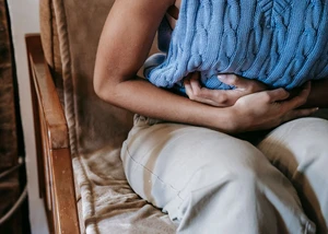 Eine Frau in einem blauen Oberteil, die sich die Hände vor dem Bauch hält
