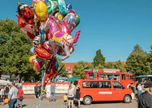 Ein Stadtteilfest während der Kieler Woche mit Luftballons, vielen Menschen und bunten Autos