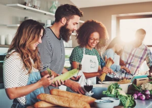 Gemeinsames Kochen in moderner Küche mit frischen Zutaten. Eine Gruppe von Menschen kocht gemeinsam in einer modernen Küche mit frischen Zutaten wie Brot, Gemüse und Pasta.