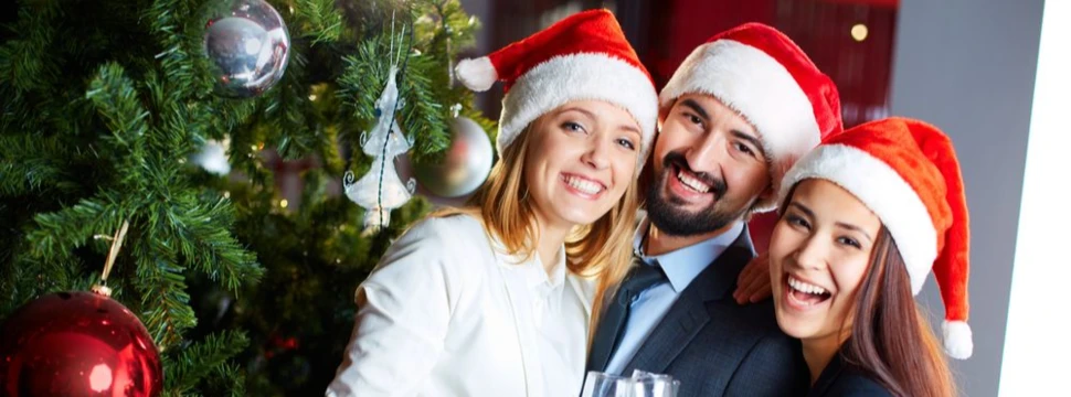 Drei Menschen mit Weihnachtsmützen neben einem geschmückten Tannenbaum