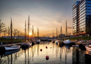 Sonnenuntergang über Segelbooten im modernen Stadthafen. Segelboote im Stadthafen bei Sonnenuntergang mit reflektierendem Wasser und moderner Architektur am Ufer.