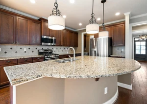 Eine Küchenzeile aus Holz mit einem Tisch aus Granit im Vordergrund und weißen Lampen darüber