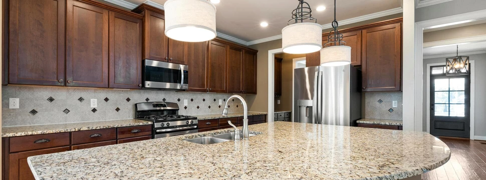 Eine Küchenzeile aus Holz mit einem Tisch aus Granit im Vordergrund und weißen Lampen darüber