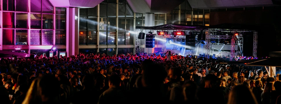 Die SpoPa Open Air ist die größte Studierendenparty Schleswig-Holsteins Feiernde Menschen vor einer Bühne an einem Gebäude mit tiefen Glasfenstern