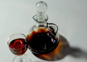 Karaffe mit dunklem Likör und ein Glas auf einer hellen Oberfläche.