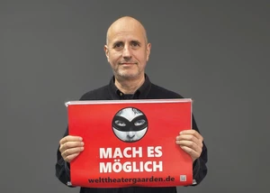 Ein Mann mit einem Plakat in der Hand vor einer dunklen Wand