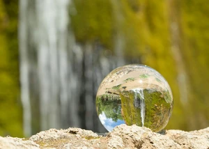 Ein Regentropfen auf einem Stein, in dem sich die Landschaft spiegelt