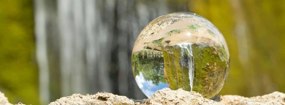 Ein Regentropfen auf einem Stein, in dem sich die Landschaft spiegelt