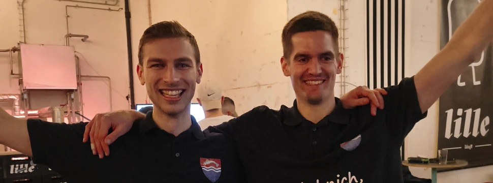 Zwei Männer in schwarzen T-Shirts, die gerade ein Darts Turnier gewonnen haben