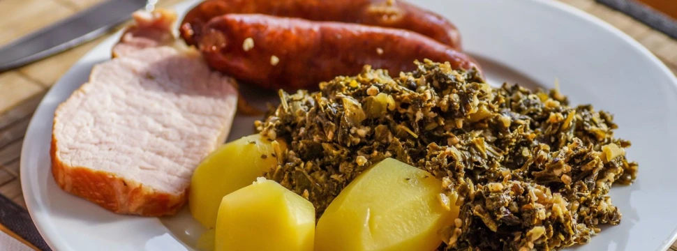 Ein Teller mit Kartoffeln, Mettenden, Kassler und Grünkohl darauf