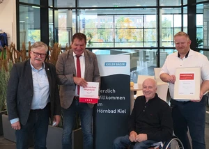 Vier Männer unterschiedlichen Alters in einem Kieler Schwimmbad mit Urkunden in den Händen