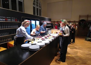 Mehrere Menschen in weißer Kleidung vor einem Tresen, auf dem Teller mit Essen zubereitet werden