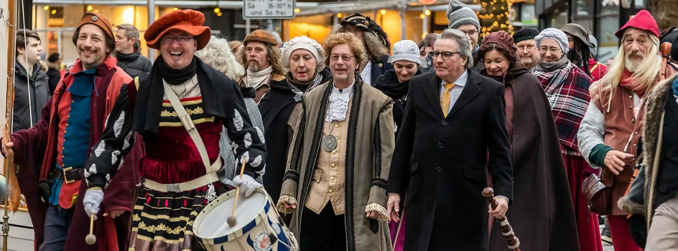Mehrere Menschen in mittelalterlicher Kleidung, die an einem Umzug in der Kieler Innenstadt teilnehmen