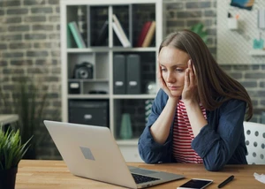 Eine Frau sitzt am Computer und hält sich die Hände über den Kopf